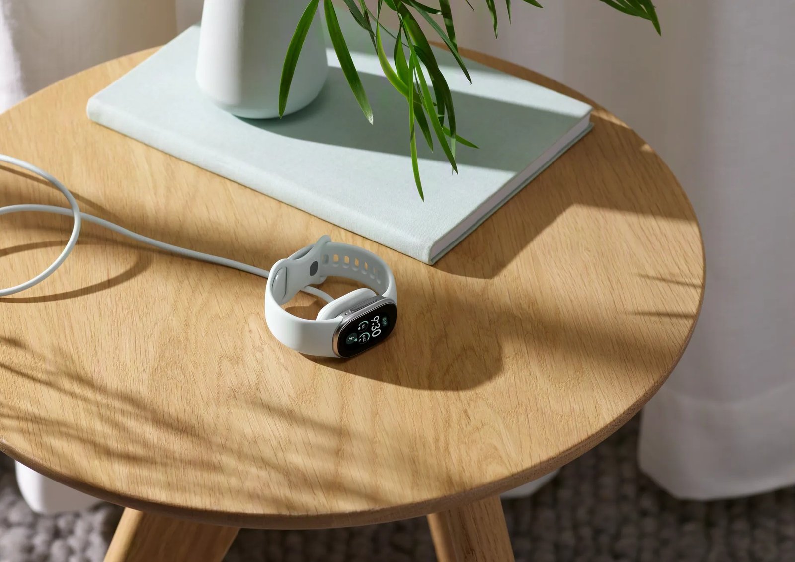 A Fitbit Edge tracker resting on a round wooden table beside a green plant
