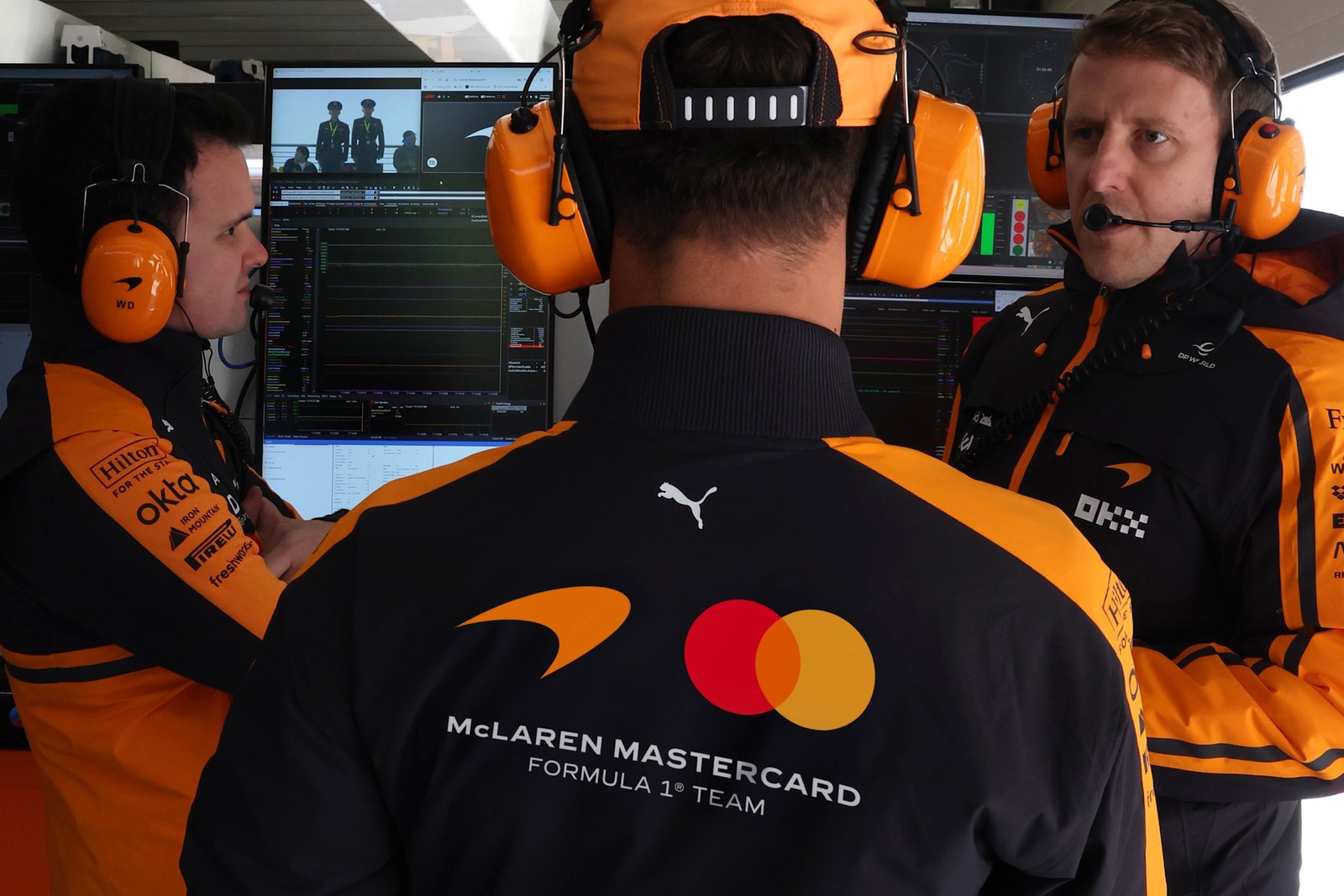 McLaren Formula 1 team engineers in the garage wearing papaya and black kit with the new wordmark
