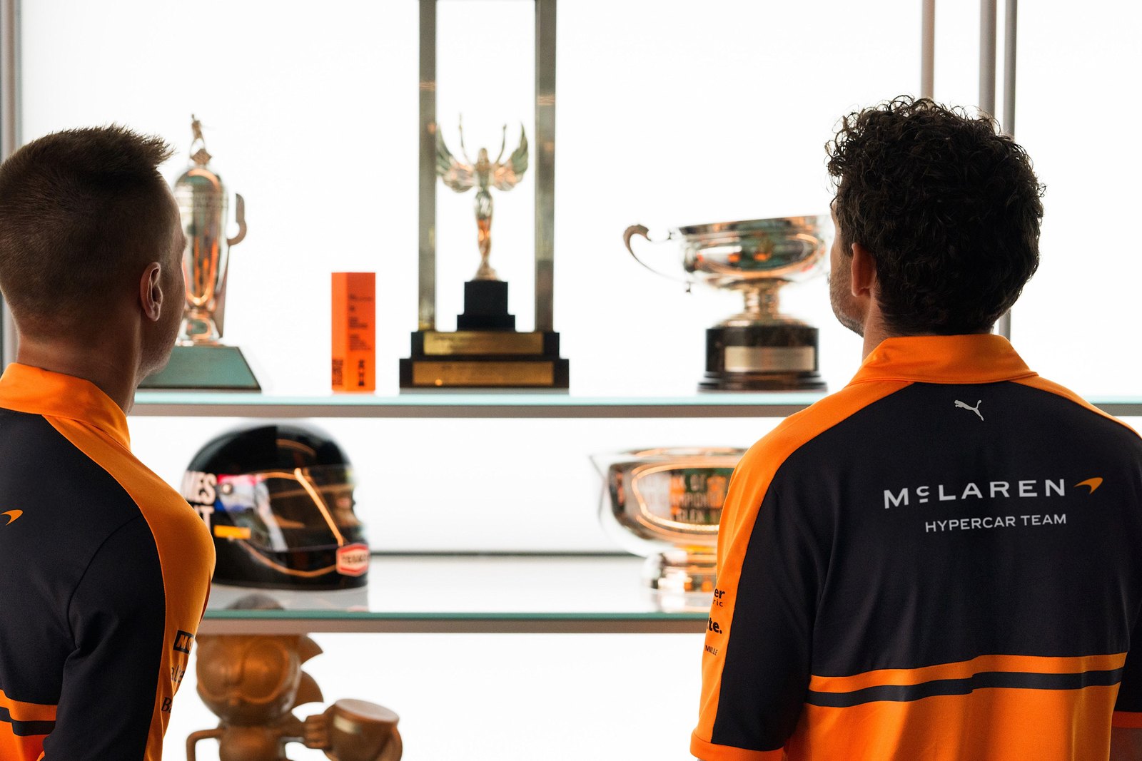 McLaren Hypercar Team members in team kit with the new wordmark beside a trophy cabinet